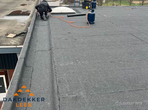 Dakdekker repareert bitumen dakbedekking op groot plat dak in Leek